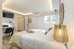 A bedroom with a bed, a desk with a laptop, a chair, a lamp, and a window.