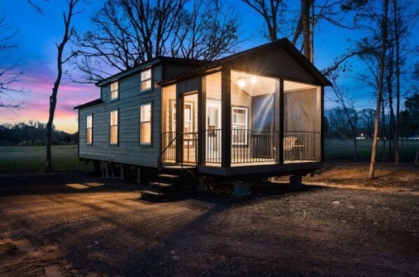 Situated on a natural setting, this cabin features a front entrance, side windows, and a porch with a railing and bench.