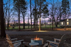 Relax in the serene outdoor seating area, surrounded by trees and a distant view, with a fire pit at its center.