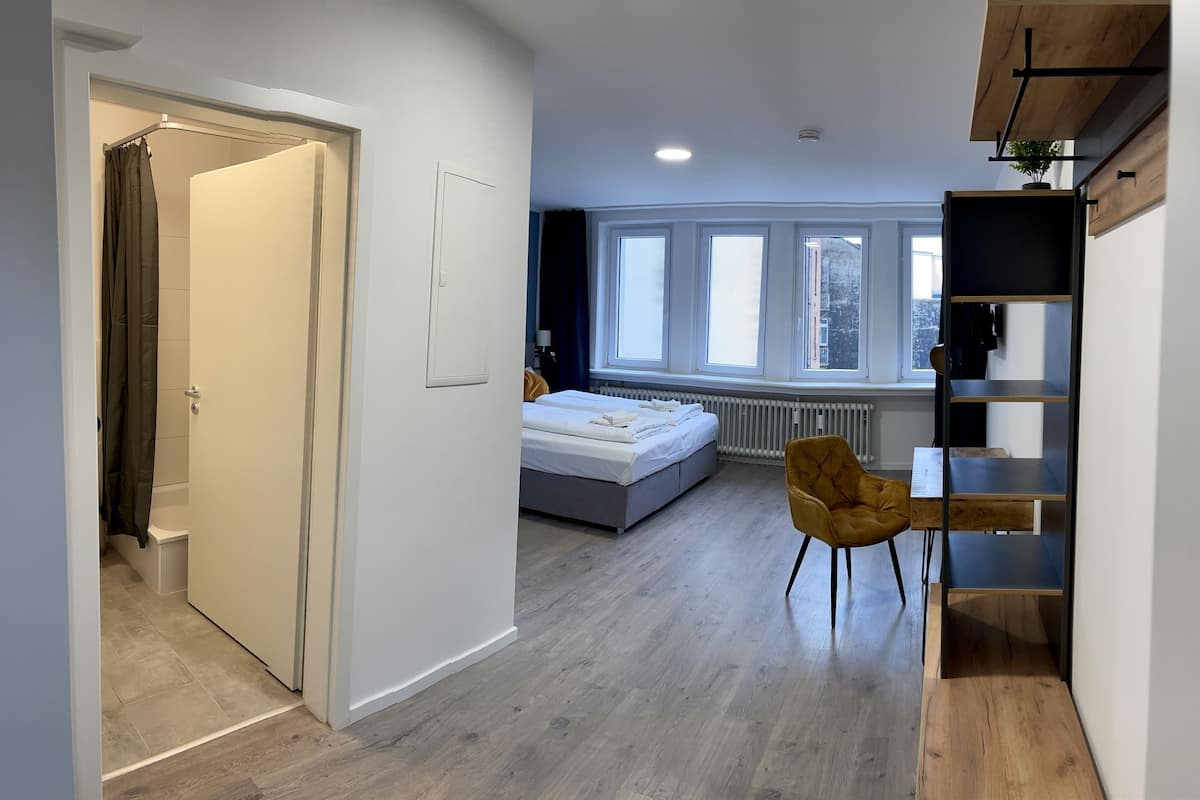 A modern bedroom with a bed, a chair, a desk, and a window with a view.