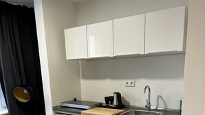 Ett kompakt kök med vita skåp, en svart bänkskiva, ett handfat och en kaffebryggare.