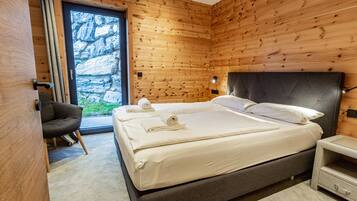 A modern bedroom with a large bed, wooden walls, a view through a glass door, and a small bedside table.