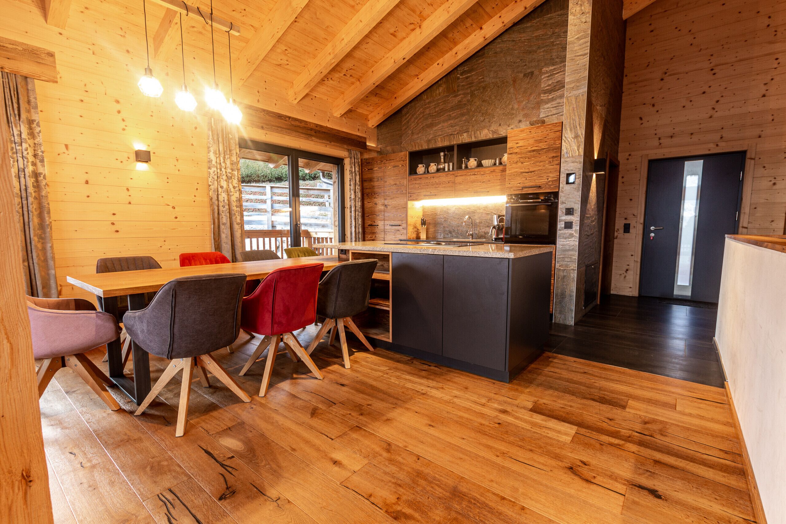 A wooden interior with a dining area, kitchen, and a door leading outside.