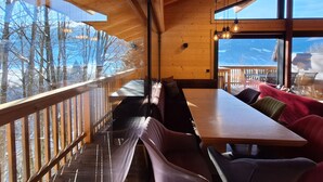 A wooden interior with a long dining table and benches, large windows with a view of snow-covered trees and mountains. - Chalet Dinkel in Niedernsill 8-B (Niedernsill)