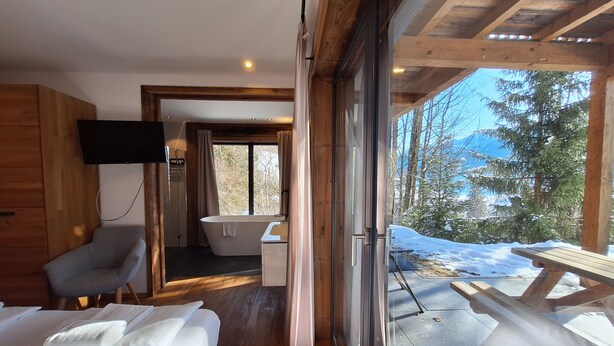 A modern cabin with a wooden interior, a bathtub, a TV, and a view of a snowy landscape. - Chalet Dinkel in Niedernsill 8-B (Niedernsill)