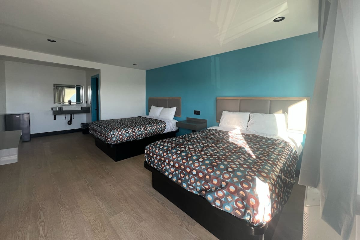 Quarto de hotel com duas camas, uma secretária pequena, um espelho e uma janela.