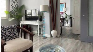 Un salon moderne avec un téléviseur, un bureau et une chaise. Une porte donne accès à une autre pièce.
