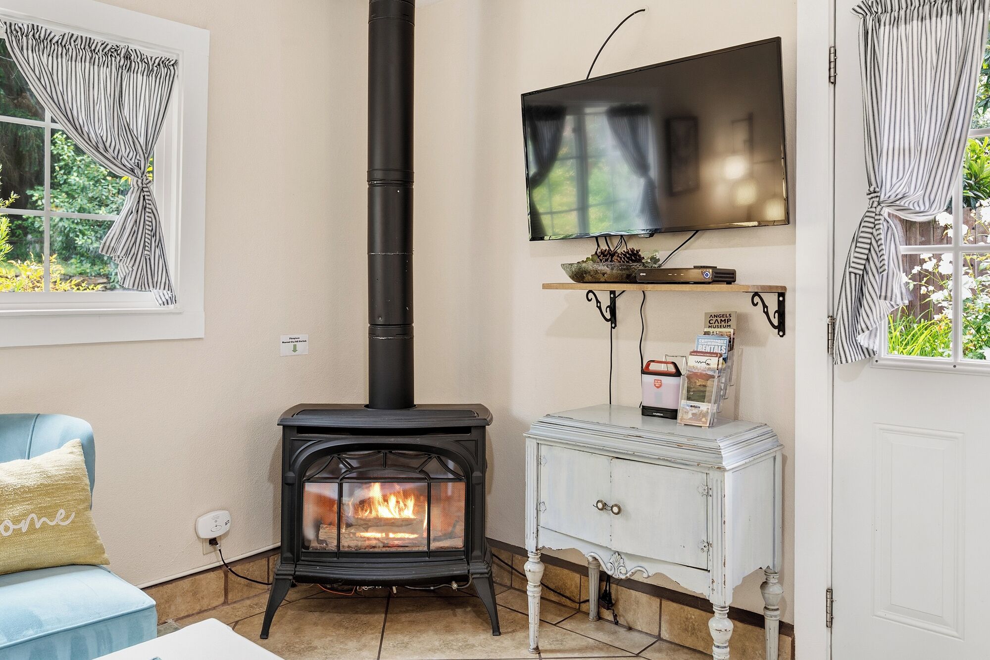Un salon doté d’un poêle à bois, d’un téléviseur fixé au mur et d’une petite table sur laquelle sont posés des magazines.