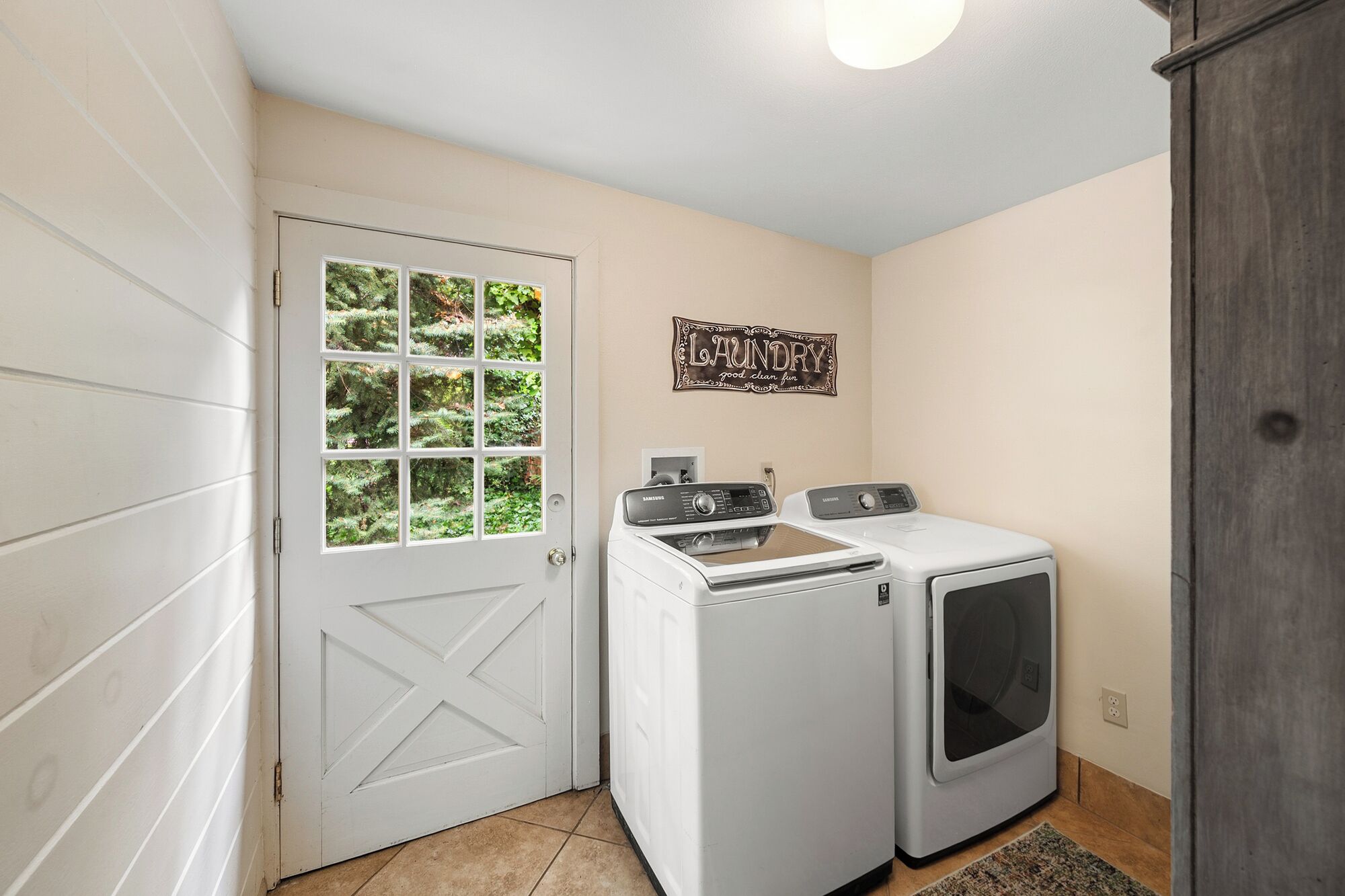 Een wasserette met twee witte wasmachines en drogers, een deur met een rasterraam, en een bord aan de muur met de tekst 'Laundry'.