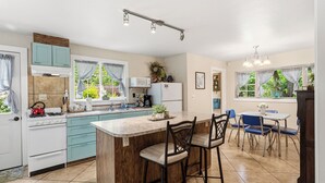 Een keuken met een centraal eiland, een eethoek met blauwe stoelen en een koelkast.