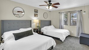 Une chambre d’hôtel avec deux lits, un ventilateur de plafond, une fenêtre avec des rideaux et une petite table avec une lampe.