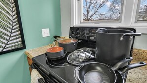 Une cuisine équipée d’une cuisinière, de casseroles, de poêles et d’une fenêtre donnant sur des arbres.
