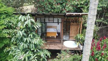 A small, rustic cabin with a wooden bed, a glass door, and a wooden deck.