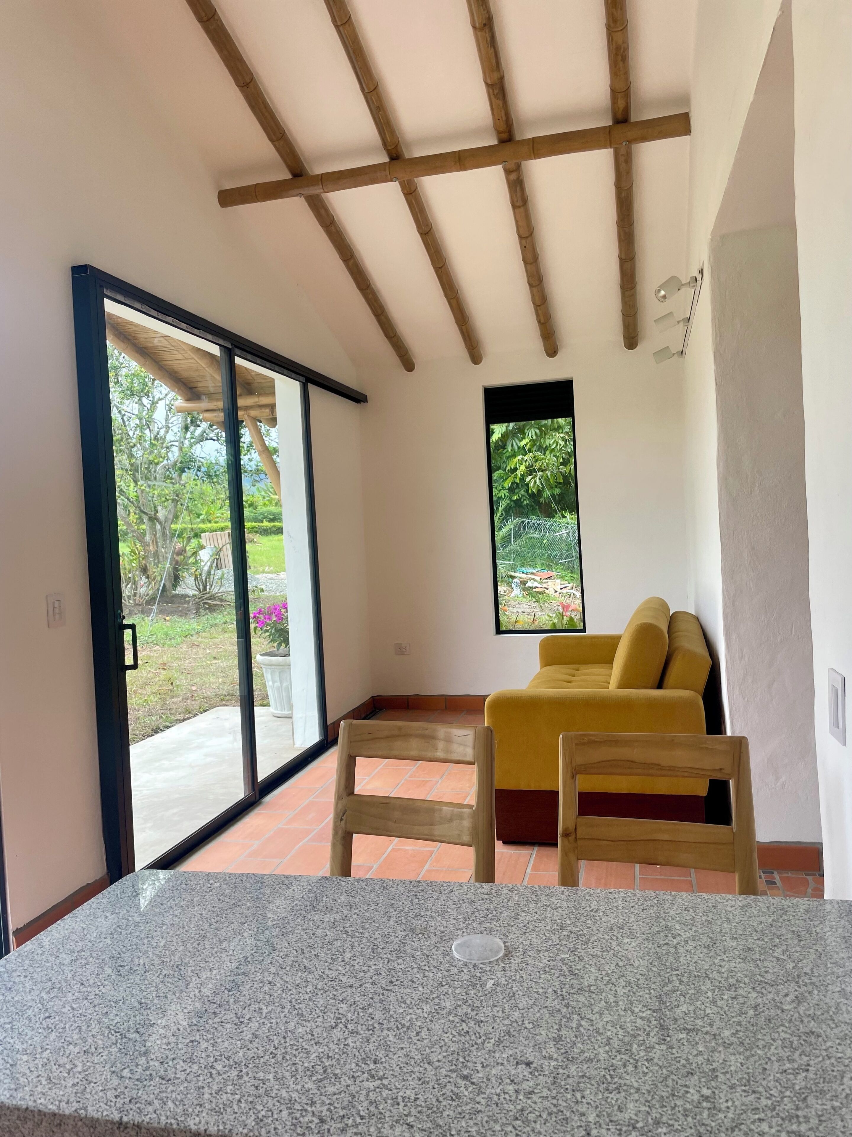 Una habitación con puerta corrediza de vidrio que da a un patio, un sofá amarillo y una silla de madera.