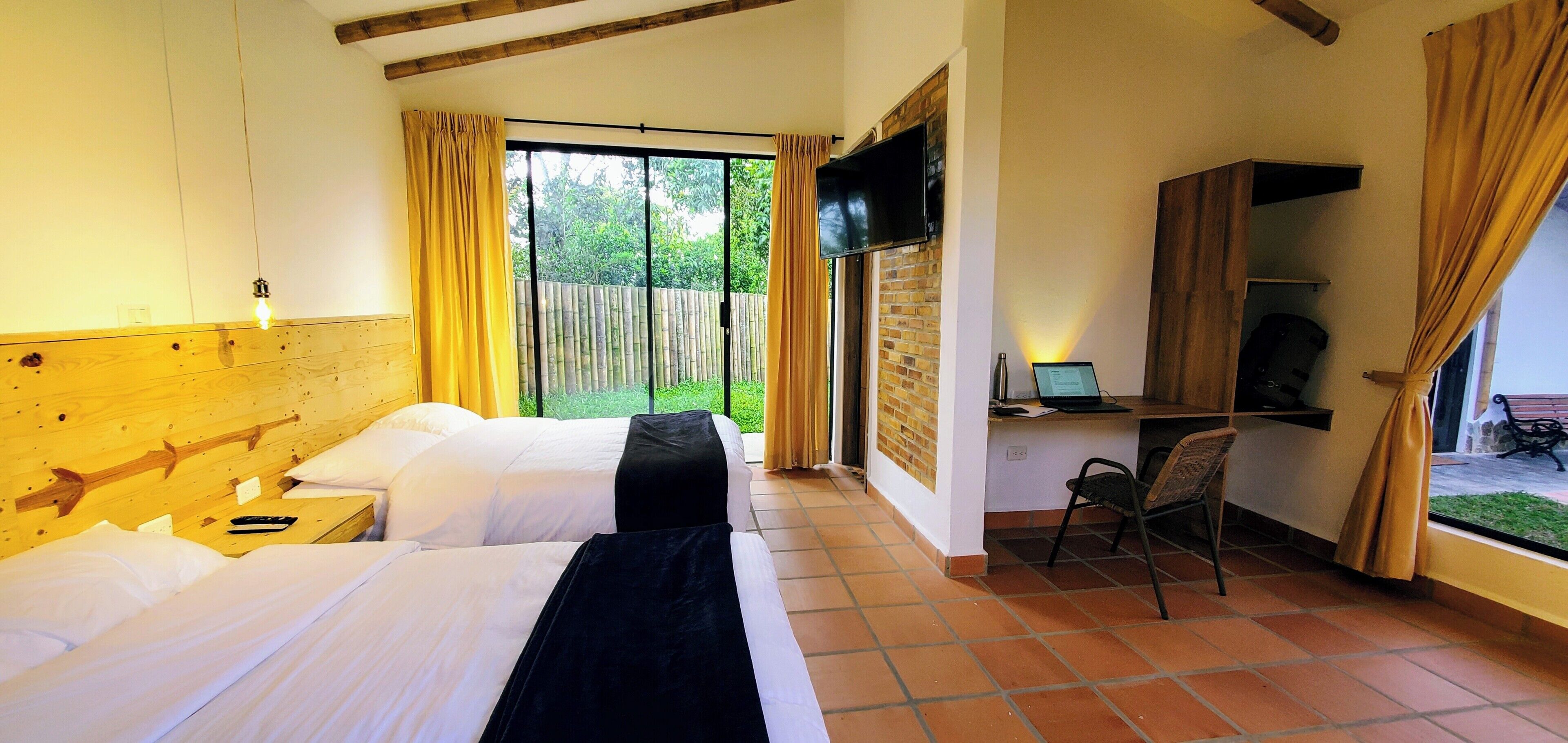 A hotel room with two beds, a desk with a computer, a TV, and a view of the outdoors.