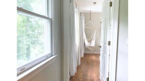 A hallway with a hammock, white curtains, and wooden flooring.