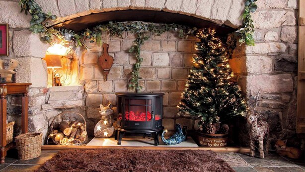 Una chimenea de piedra con un árbol de Navidad, un estufa de leña y adornos festivos.