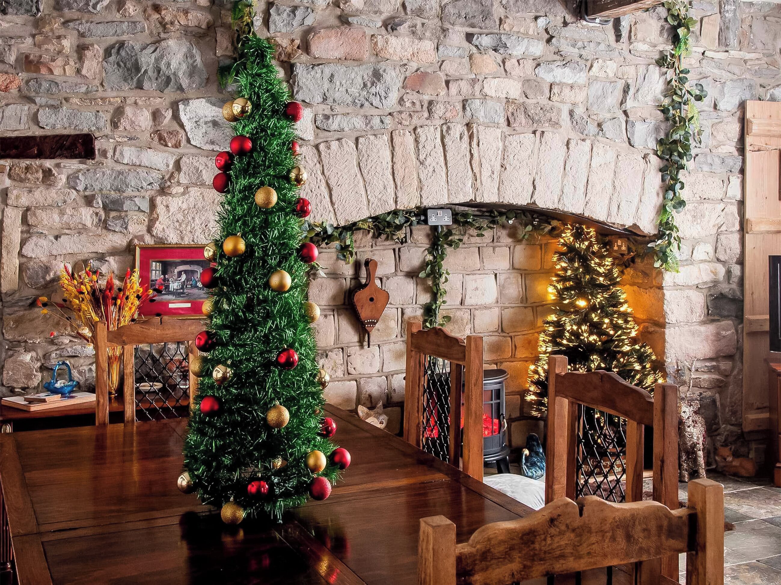 Eine rustikale Steinwand, ein Holztisch und ein Weihnachtsbaum mit Schmuck.
