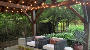An outdoor patio with wicker furniture, string lights, and a potted plant. - Cozy Cabin with fireplace, hot tub & hiking trails (Richmond)