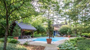 A backyard with a swimming pool, a covered seating area, and various plants. - Cozy Cabin with fireplace, hot tub & hiking trails (Richmond)