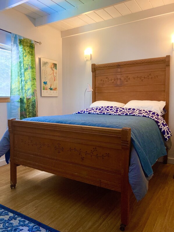 A wooden bed with a floral headboard, a blue and white patterned bedspread, and a blue and white patterned throw blanket.