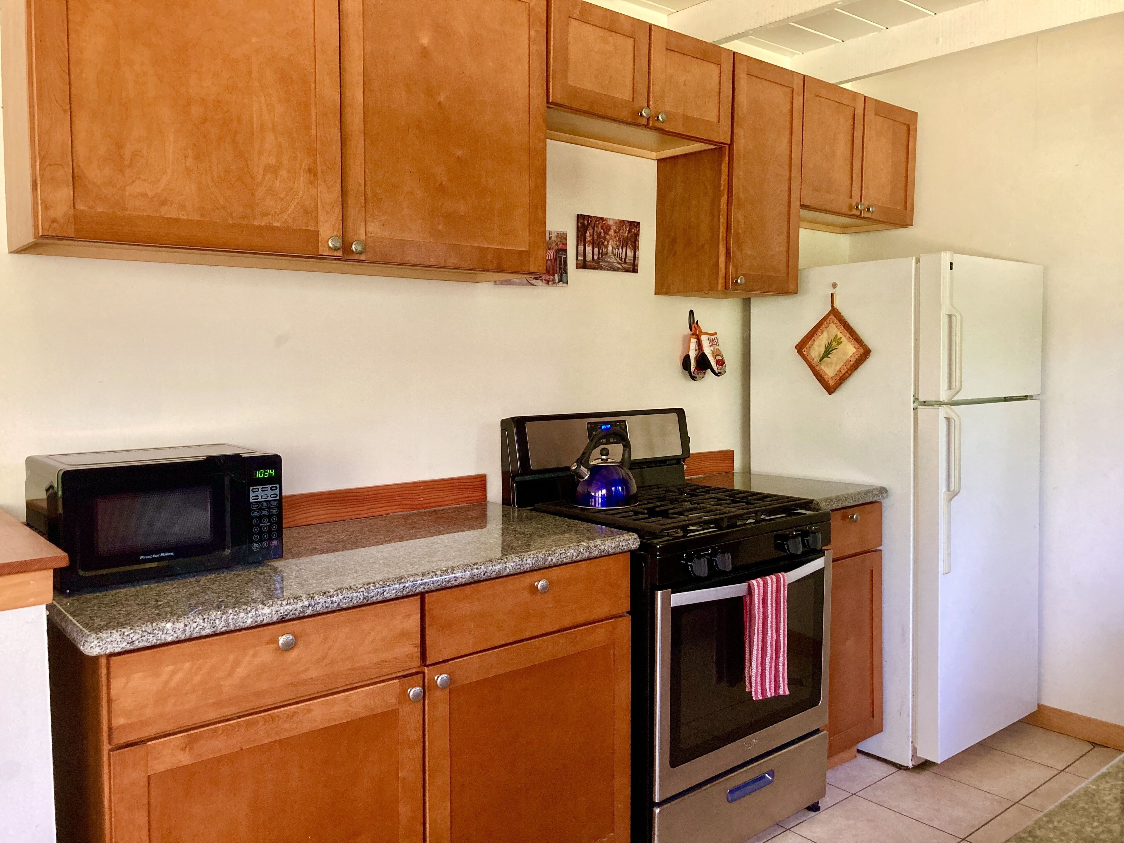Una cocina con gabinetes de madera, microondas, cocina a gas y refrigerador.