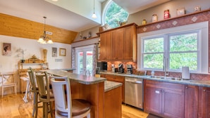 A kitchen with wooden cabinets, a stainless steel dishwasher, and a large window. - Luxury Home, Stunning Views!, One-Level, Near Main St., Privacy, FirePit & More (Waynesville)