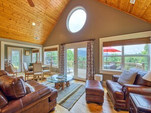 A spacious living room with leather sofas, a glass coffee table, and a view of a deck.