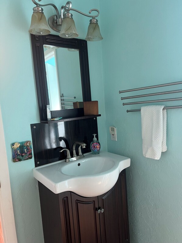 A bathroom with a white sink, dark wooden cabinet, and a mirror with two light fixtures. - Spacious 2-Bedroom Townhome Steps Away From Beach (St. Augustine)