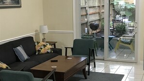 En stue med sofa, sofabord og lampe. Der er en skydedør til et udendørs område med grill og havemøbler.