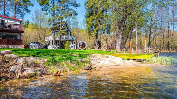 Una cabaña junto al lago con un balcón, una estructura circular de cristal y un pequeño bote.