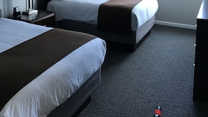 Habitación de hotel con dos camas, ventilador de techo, ventana con cortinas y un escritorio.