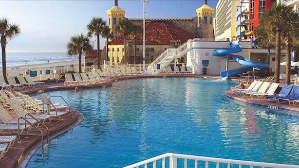 Un área de piscina con tumbonas, un tobogán de agua y un edificio con tejado de tejas rojas.