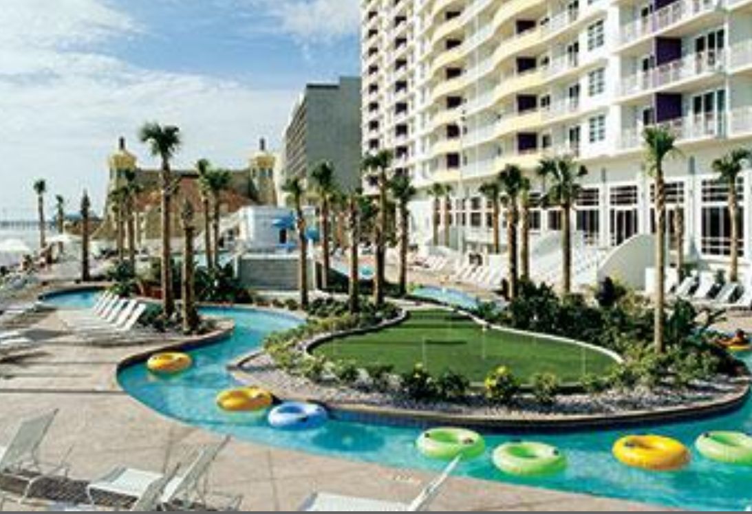 A resort pool area with multiple water slides, lounge chairs, and a large building with balconies.