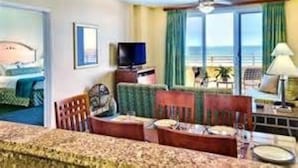 Habitación de hotel con cama, sofá, televisión y balcón con vista al océano.