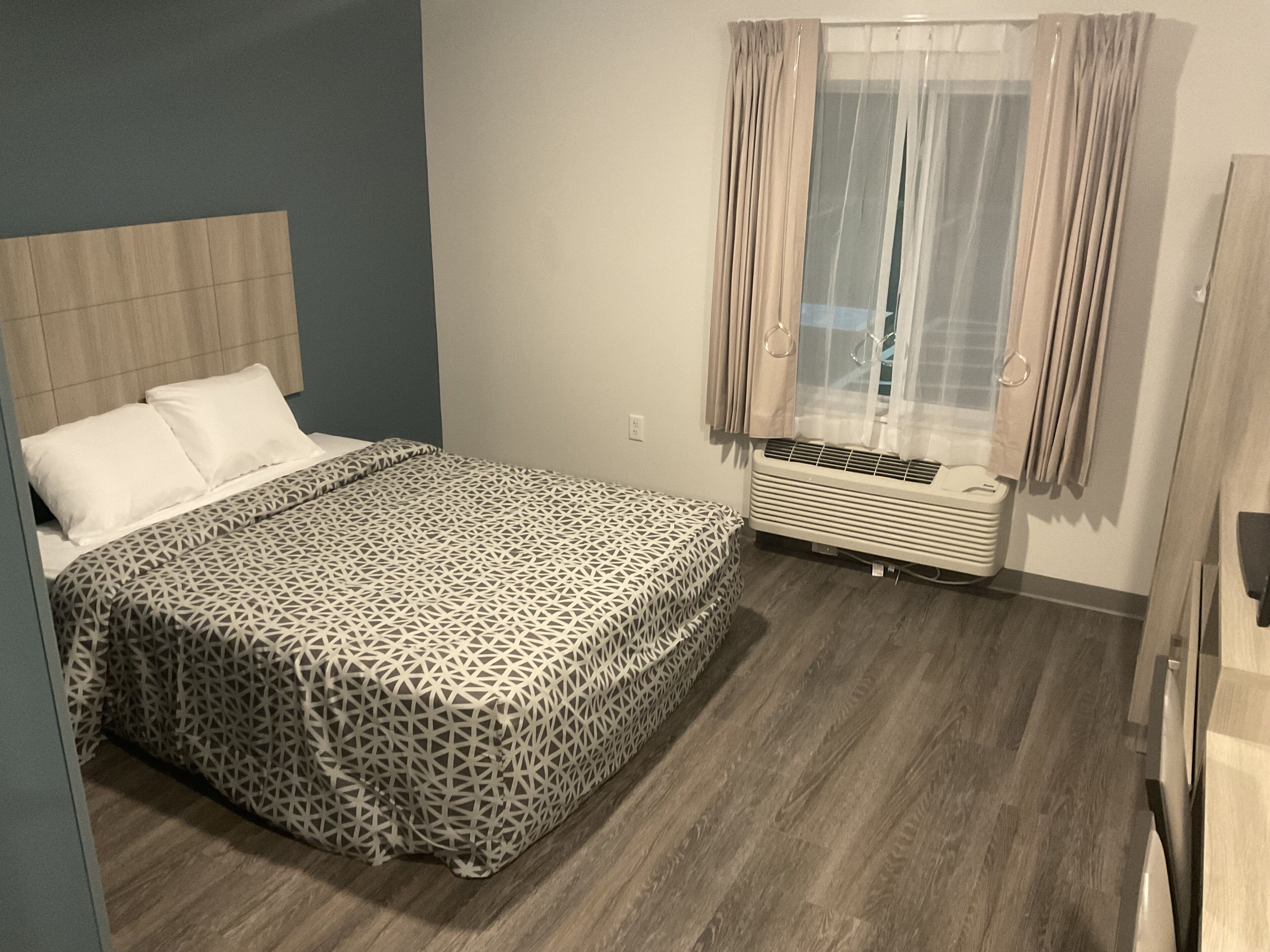 A bedroom with a bed, a window with curtains, a heater, and a wooden floor.
