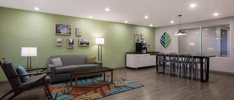 A modern living room with a sofa, coffee table, and chairs, a dining area with a table and chairs, and a kitchen area with cabinets and appliances.