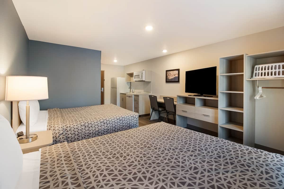 A hotel room with two beds, a desk, a chair, a TV, and built-in shelving.