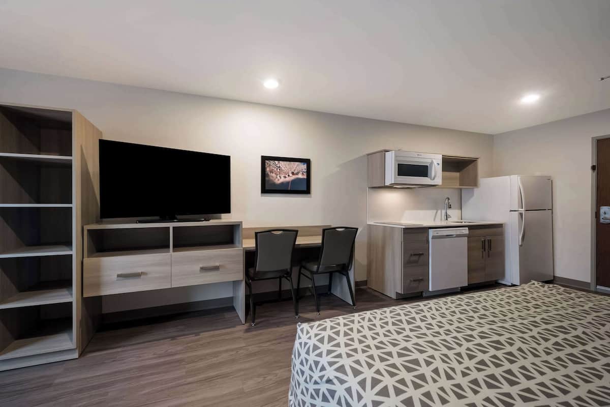 A compact room with a bed, a TV, a desk with chairs, a microwave, and a refrigerator.