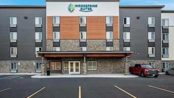 A multi-story hotel with a modern design, featuring a mix of wood and stone facades, and a parking lot with marked spaces.