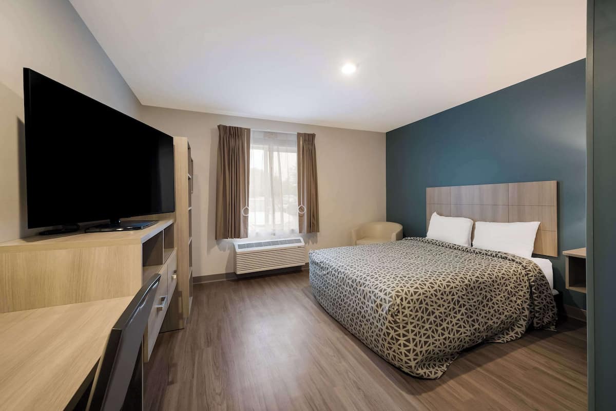 A hotel room with a bed, a TV, a desk, and a window with curtains.