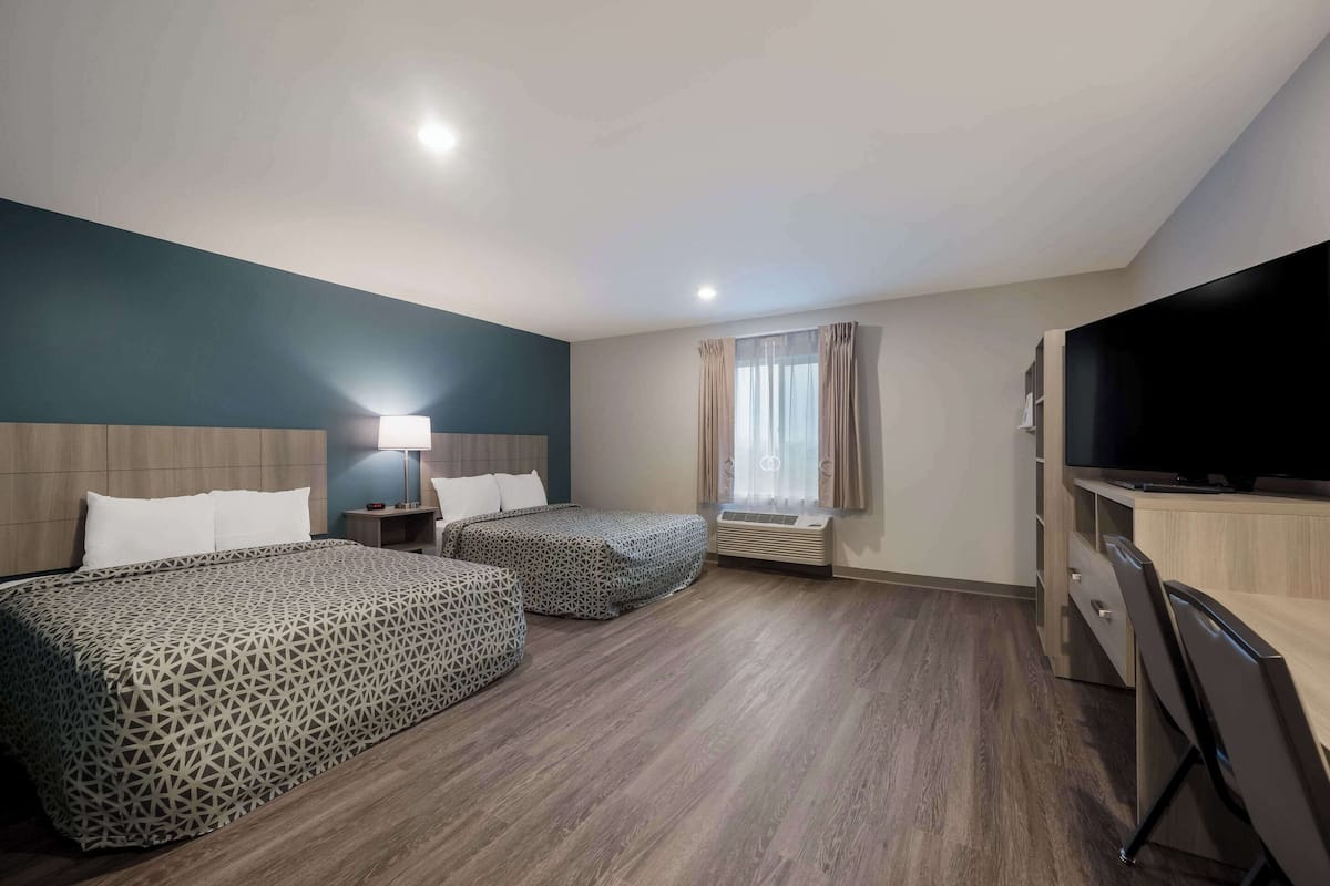 A hotel room with two beds, a desk, a television, and a window with curtains.
