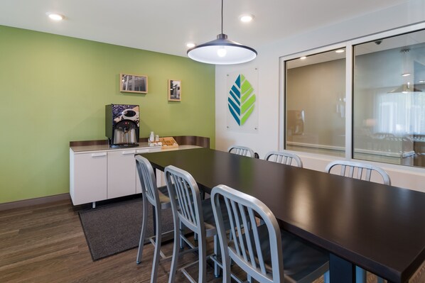 A conference room with a long table, chairs, a coffee machine, and a large window.