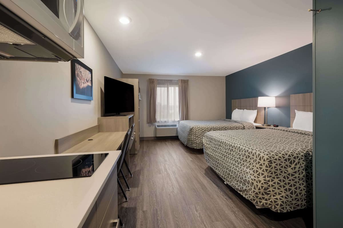 A hotel room with a desk, two beds, a TV, and a window with curtains.