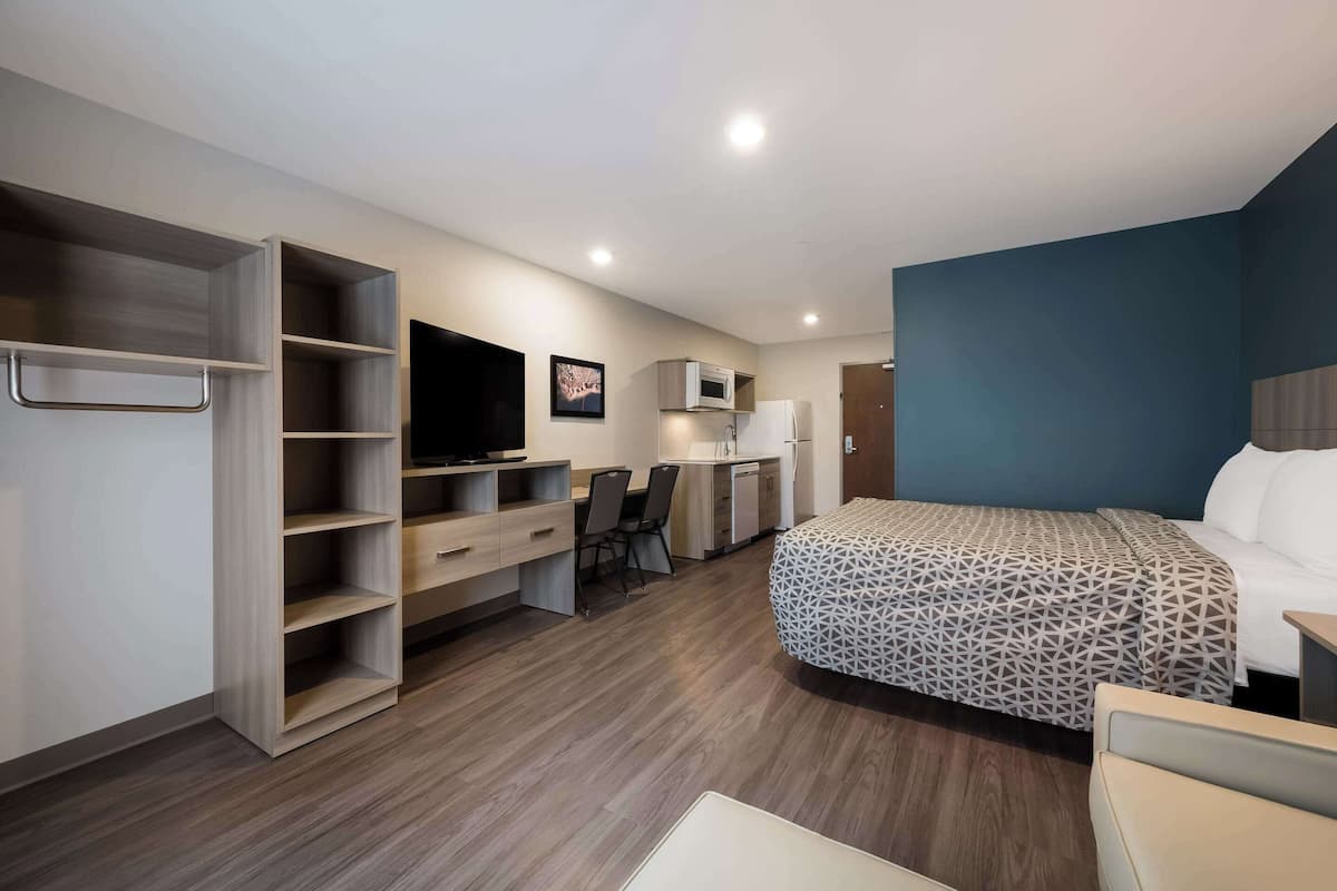 A hotel room with a bed, a desk, a chair, a wardrobe, and a television.