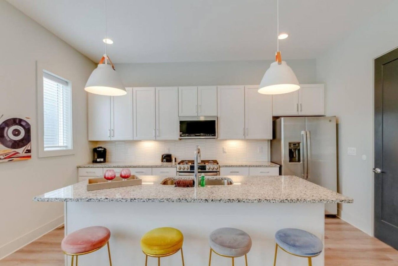 A modern kitchen with white cabinets, a central island with stools, and pendant lighting.