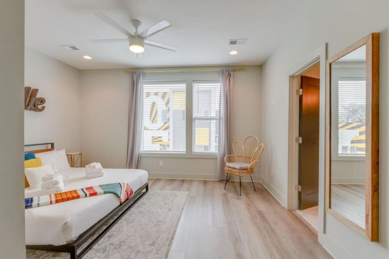 Une chambre à coucher avec un lit, une chaise, un ventilateur de plafond et une fenêtre avec des stores.