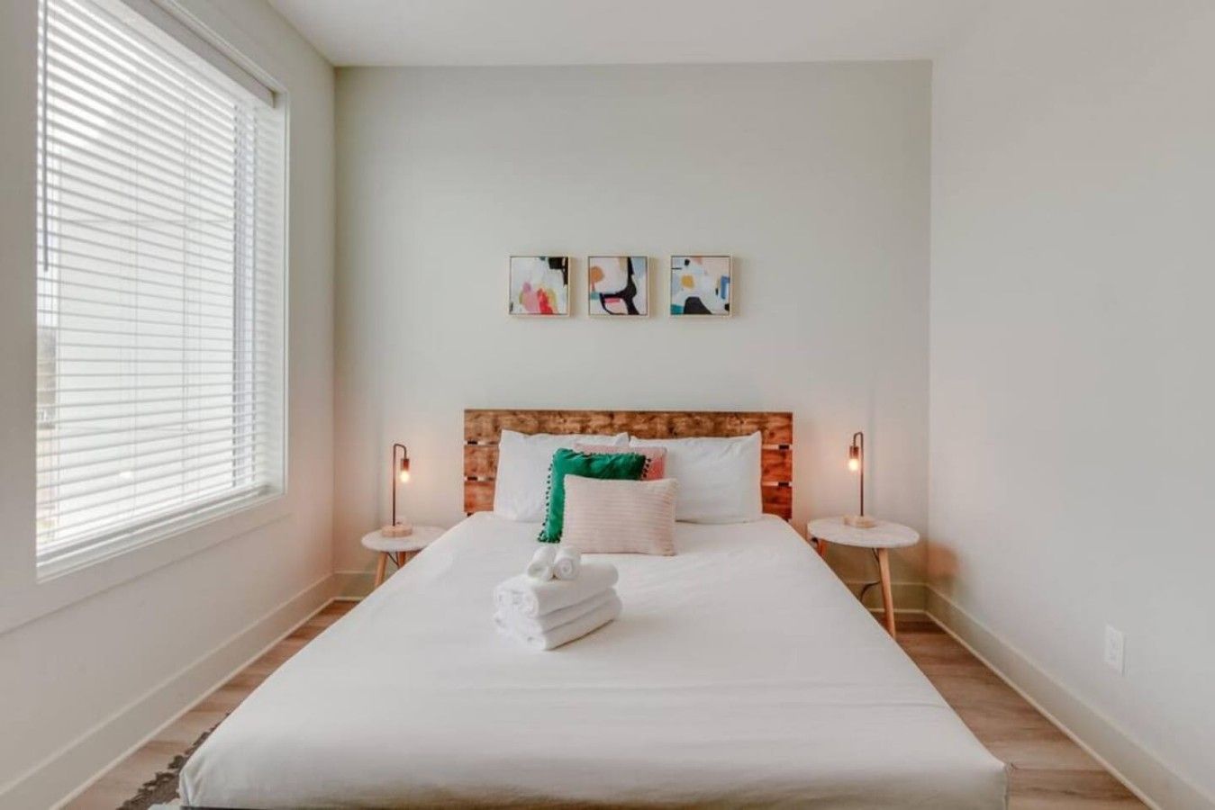 A hotel room with a large bed, two bedside tables, a wooden headboard, and artwork on the wall.