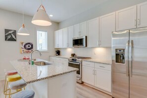 Una cocina moderna con armarios blancos, electrodomésticos de acero inoxidable, encimera de granito e iluminación colgante.
