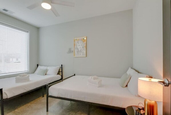 A room with two single beds, a ceiling fan, a framed picture on the wall, and a bedside lamp.